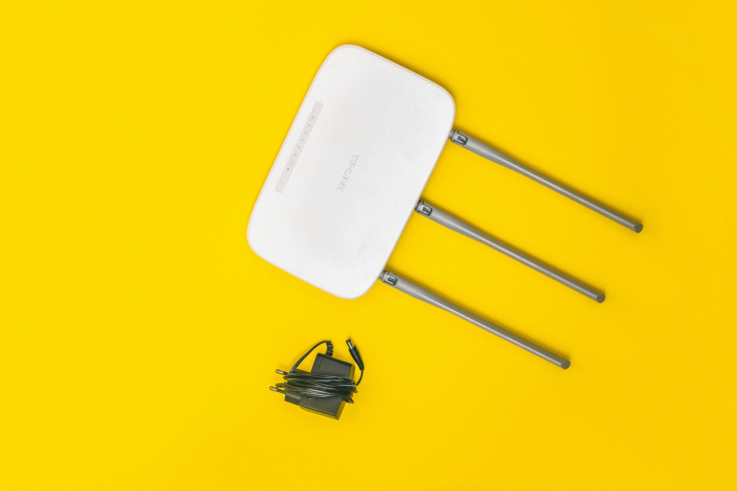 White router with three antennas and cables on bold yellow background, ideal for tech concepts.